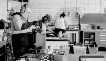 Workers dismantling electronic devices on workbenches with tools and components inside an e-waste recycling facility
