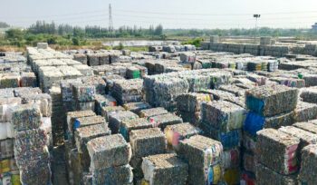 Stacks of compressed plastic waste bales arranged in rows at an outdoor recycling facility, illustrating global waste ban challenges