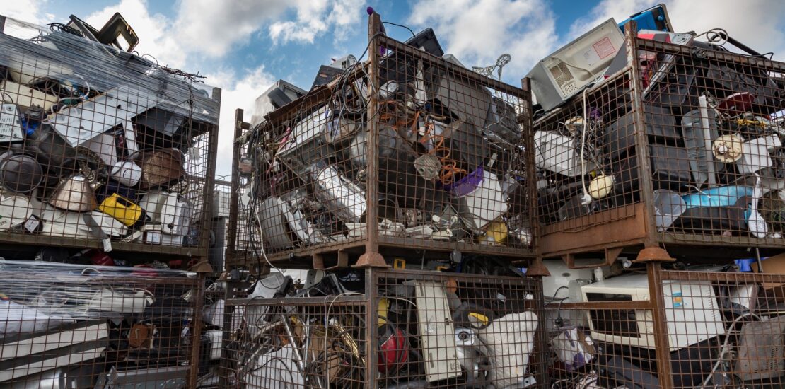 Large metal cages filled with discarded electronics including monitors, printers, and cables at an e-waste recycling facility.