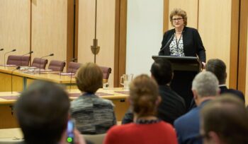 Speaker at a podium presenting to an audience in a formal conference room at Parliament House during ANZRP white paper launch.