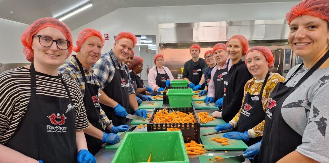 ANZRP team volunteering at FareShare 2024, wearing aprons and red hairnets while chopping carrots in a commercial kitchen.