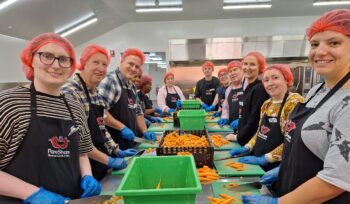ANZRP team volunteering at FareShare 2024, wearing aprons and red hairnets while chopping carrots in a commercial kitchen.