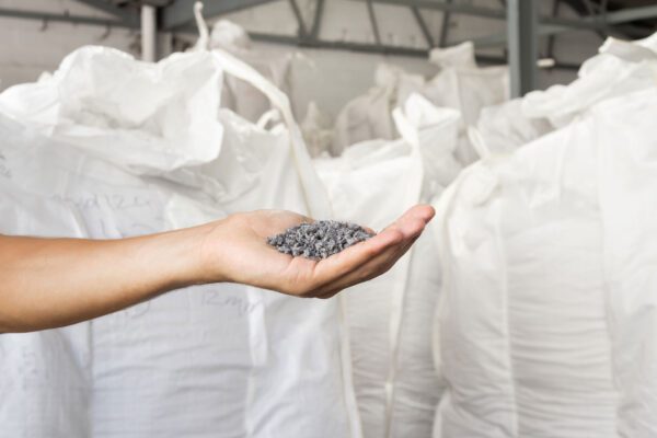 Recycled plastic granules held by hand inside an industrial facility, used in practical e‑waste solutions for circular construction and manufacturing.
