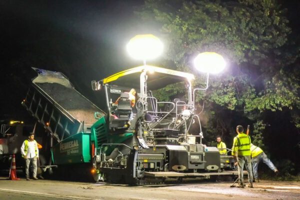 Night roadwork scene with an asphalt paving machine laying Resin8‑modified asphalt mix in Mexico and Costa Rica, demonstrating practical e‑waste solutions for sustainable roads.