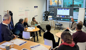 ANZRP customer experience workshop with employees seated around tables, virtual presentation screen, handouts, and wall charts.
