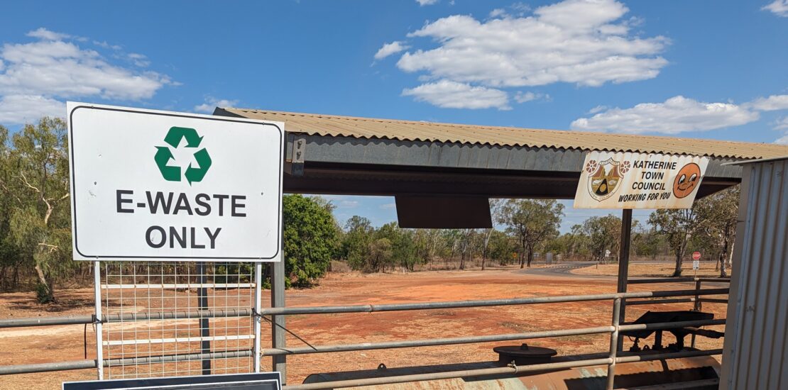 Outdoor e-waste drop-off at Katherine Town Council with ‘E-WASTE ONLY’ sign, metal roof, banner, and clear blue sky.