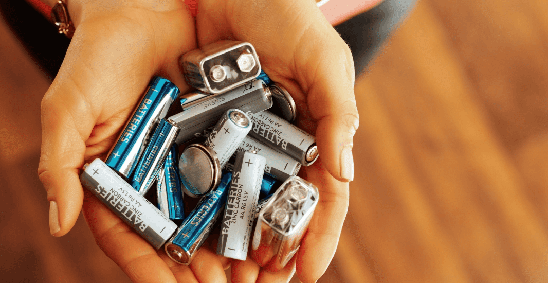 Hands holding used household batteries, representing e‑waste and battery recycling.