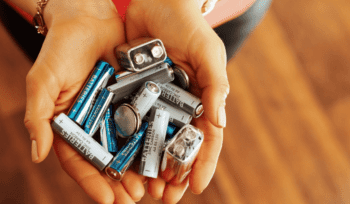 Hands holding used household batteries, representing e‑waste and battery recycling.