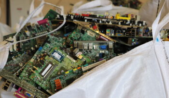 Bulk bag filled with dismantled green circuit boards and electronic components collected for e-waste recycling at facility.
