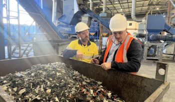 ANZRP Operations and Compliance Manager inspecting shredded e-waste plastics at Total Green Recycling facility with blue machinery.