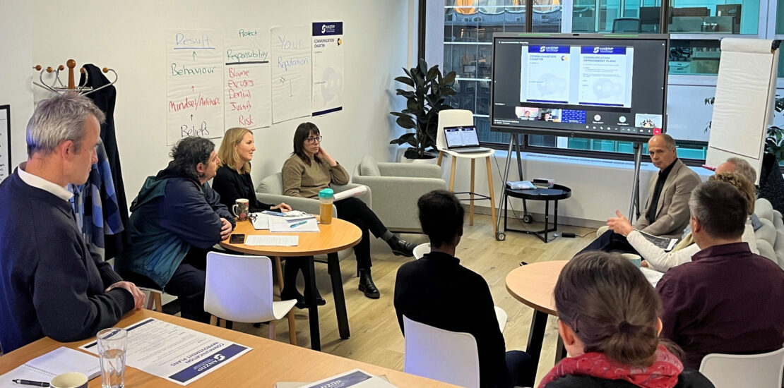 ANZRP customer experience workshop with employees seated around tables, virtual presentation screen, handouts, and wall charts.