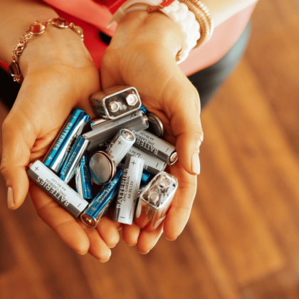 Close-up of hands holding a collection of used batteries, including AA, AAA, and rectangular 9V batteries, in silver and blue colours, representing battery recycling and safe disposal practices.