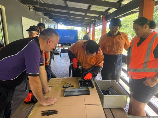 rarotonga island e-waste management training Rarotonga Island e-waste management training session showing participants in safety vests dismantling electronic devices on a table, with tools and components visible.