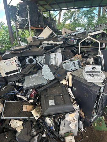 samoa island e waste low Pile of discarded e-waste under a covered area in Samoa, including old monitors, printers, cables, and appliances for recycling.
