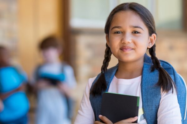 the laptop initiative 23 Child with backpack holding a notebook in a school setting, representing The Laptop Initiative for education and digital inclusion.